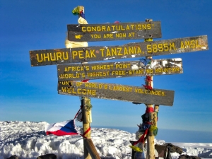 Η θρυλική ξύλινη πινακίδα στην κορυφή Uhuru του Kilimanjaro στα 5.895 μέτρα, κάτω από γαλανό ουρανό.