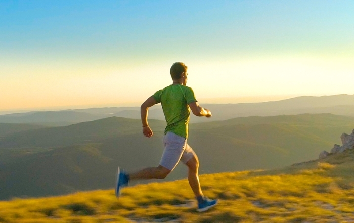 Ορειβάτης σε προπόνηση trail running τρέχει σε μονοπάτι βουνού στο ηλιοβασίλεμα